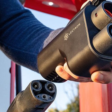 A person holding a Lectron Vortex Plug NACS to CCS adapter next to a Supercharger cable.
