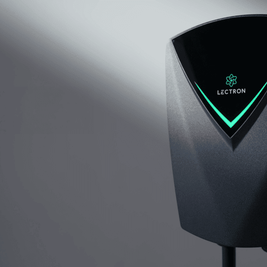 A close-up of the Lectron Nexus mounted on a gray wall, a glowing green V-shaped status light indicator on its front panel.