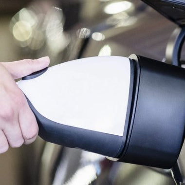 A hand holding a white Lectron charging adapter plugged into the charging port of a dark-colored electric vehicle.
