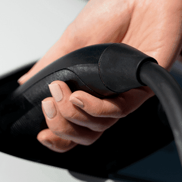 A hand plugs a Lectron NACS EV charger into a white EV.